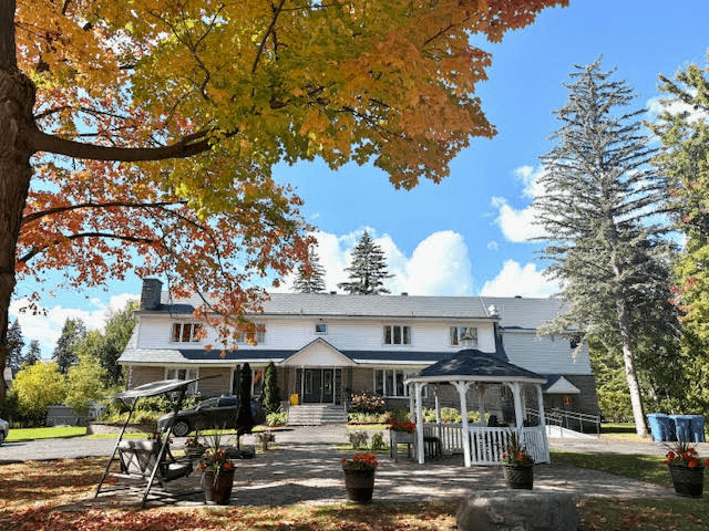 Manoir Beaconsfield residence in autumn, with a stone patio, gazebo, and trees framing the house
