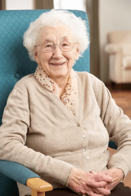 A smiling resident in a cardigan, seated in an armchair in a warm, homelike setting